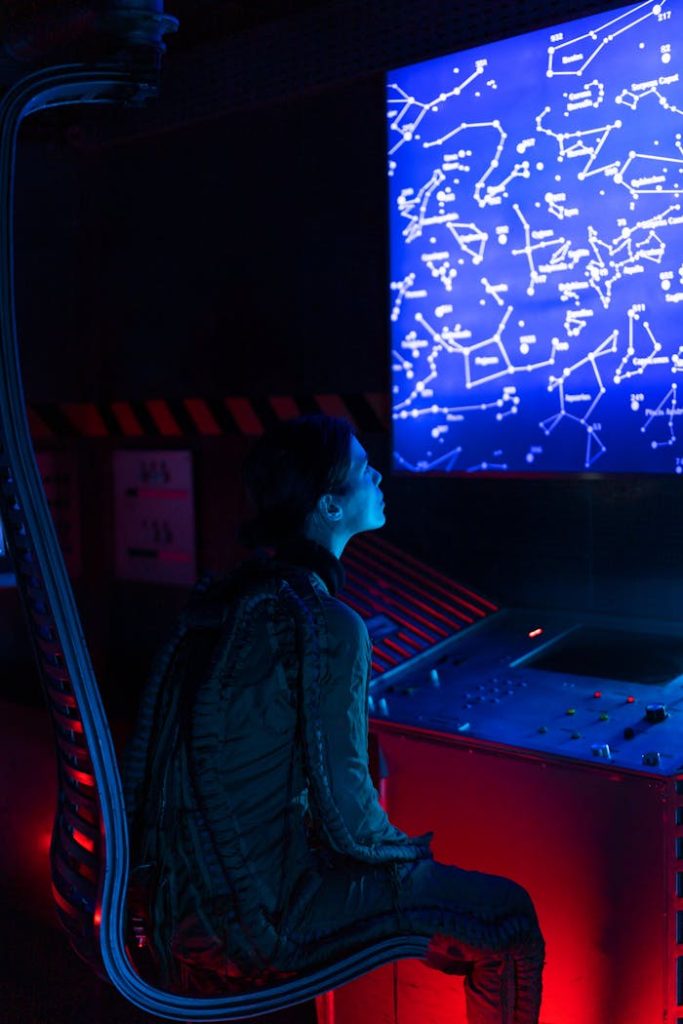 A woman in a space suit studies a futuristic control panel displaying star constellations.